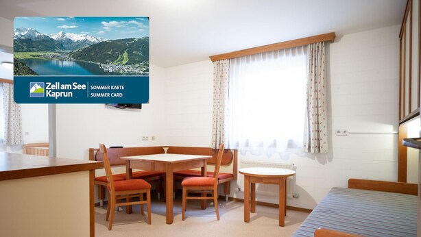 A room with a wooden table and chairs, a bed with a striped bedspread, and a window with curtains. - Seilergasse Apartments - TOP 7 (Zell am See)