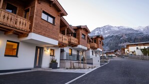 A row of wooden buildings with balconies, a paved street, and mountains in the background. - First IN Mountain Chalet B (Kaprun)