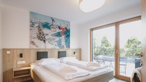 A modern bedroom with a wooden headboard, a large bed, a painting of a ski lift, and a sliding glass door to a balcony. - First IN Mountain Chalet B (Kaprun)