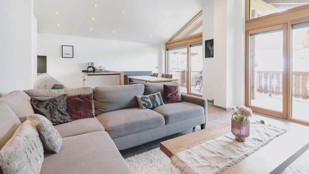 A modern living room with a sofa, coffee table, and a dining area with a table and chairs. - First IN Mountain Chalet B (Kaprun)