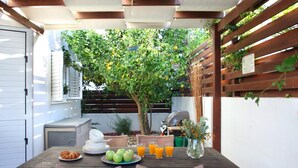 Une terrasse extérieure avec une table en bois mise pour le petit-déjeuner, comprenant des croissants, des pommes et du jus d’orange.