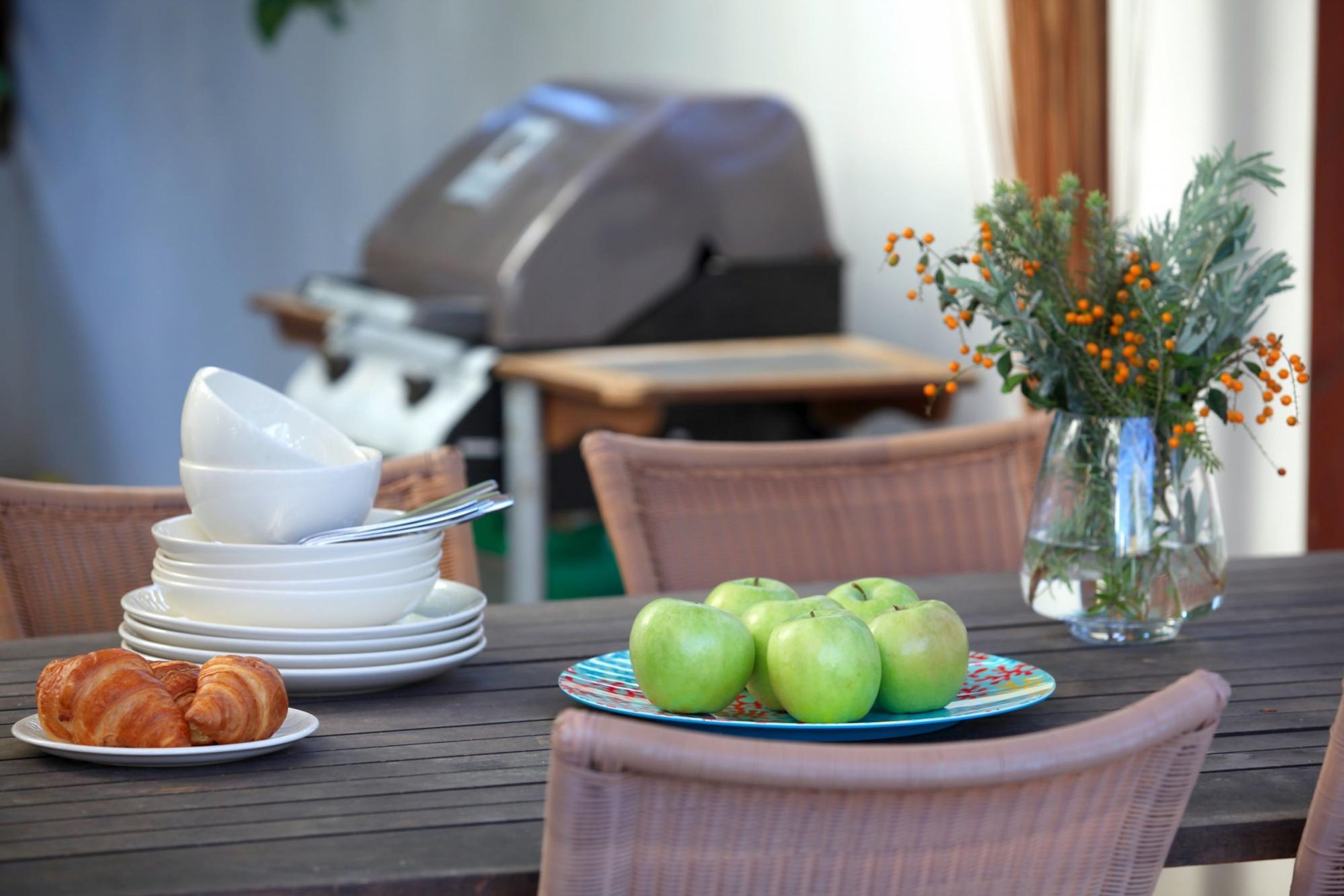 Een eettafel met borden, een vaas met bloemen en een barbecue op de achtergrond.