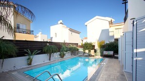 Une piscine dotée d’une terrasse carrelée, entourée d’un petit muret et agrémentée de plantes en pot.
