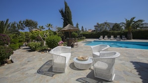 A poolside area with white wicker furniture, a stone patio, and a clear blue pool. - Mazeri in Protaras With 5 Bedrooms and 4 Bathrooms (Ayia Napa)