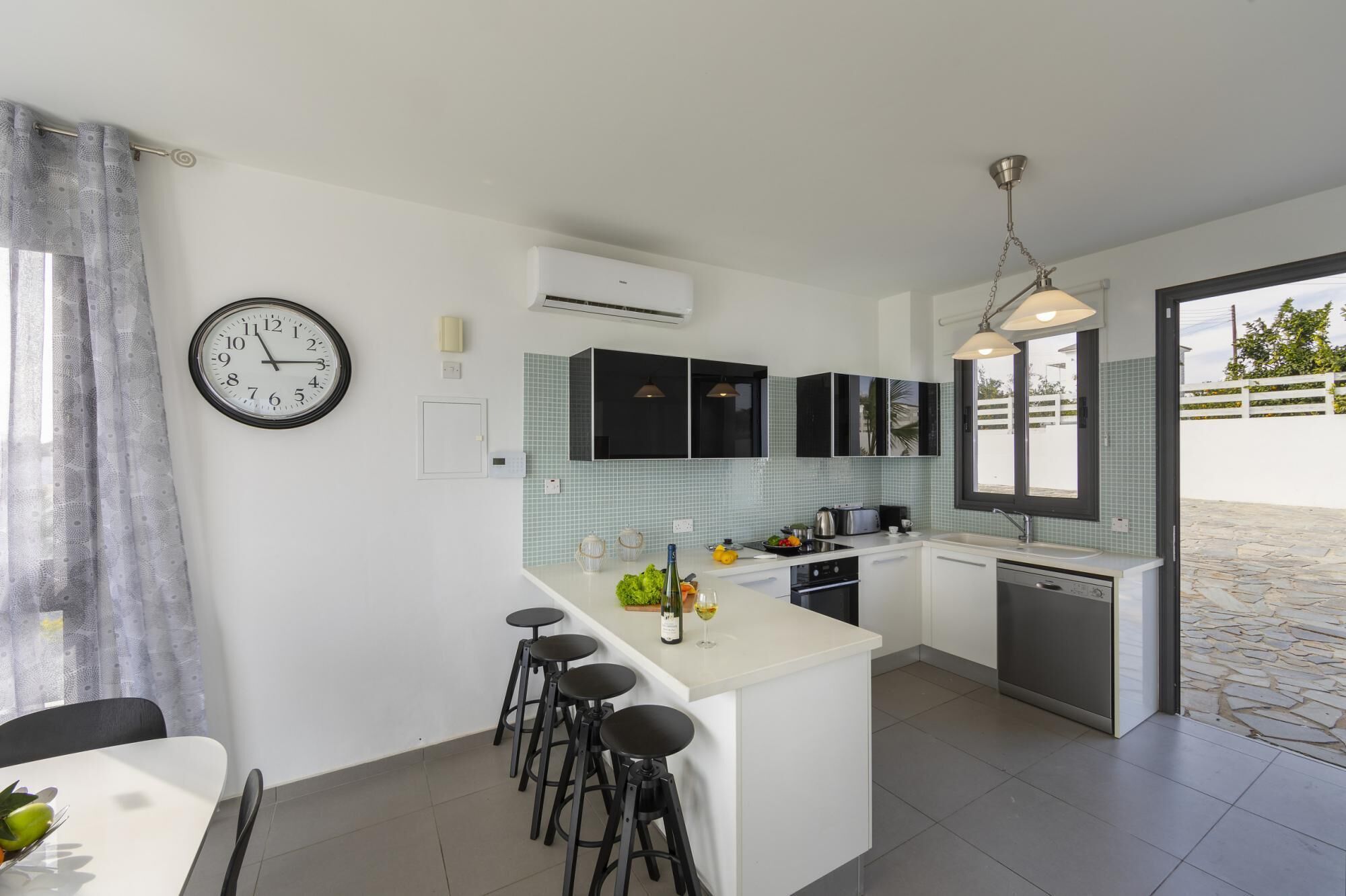 A modern kitchen with a central island, black cabinets, a clock, and a view to the outside.