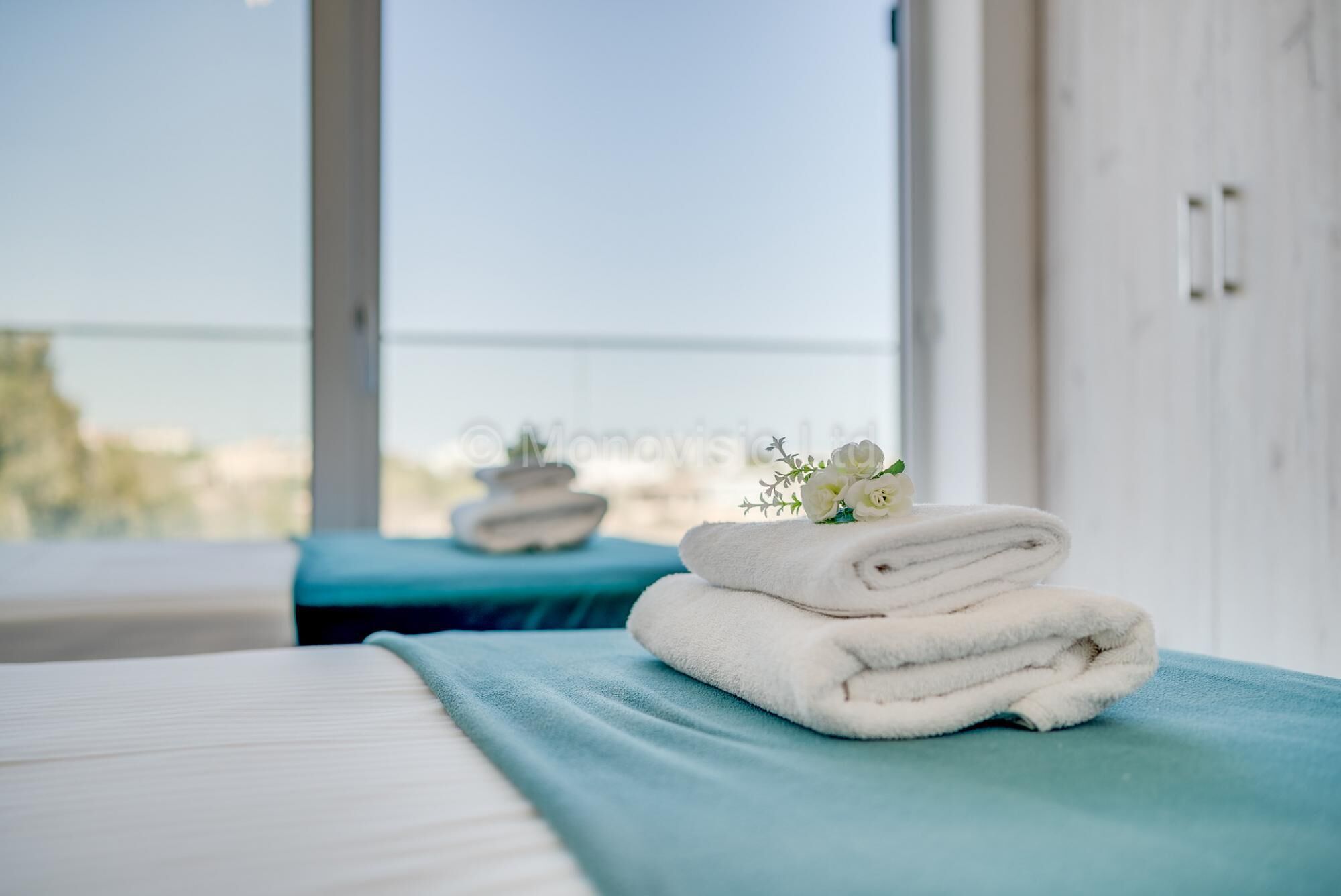 A hotel room with a bed, a blue bedside table, and a window with a view.