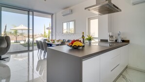 A modern kitchen with a large island, a dining area with chairs, and a view of the outdoors. - Protaras Olivine Pearl Villa 16 (Paralimni)