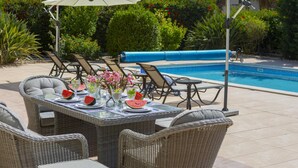 Un espace extérieur avec une piscine, des meubles en osier, une table garnie de tranches de pastèque et de fleurs, et des parasols pour créer de l’ombre.