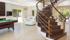 Un salon moderne doté d’un escalier à volutes, d’une table de billard et d’un coin salon avec un canapé blanc et une table à manger.