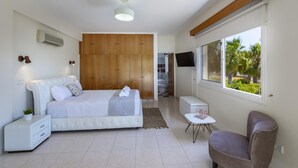 Une chambre moderne avec un grand lit, une armoire en bois, une télévision et une fenêtre donnant sur des palmiers.