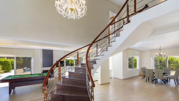 Un vaste espace de vie agrémenté d’un magnifique escalier, d’une table de billard et d’un coin repas avec des chaises.
