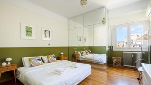 A modern bedroom with a large bed, a dresser, a mirror, and a window with a view of buildings. - 3 Bdrm Luxury Apt Incredible Acropolis View (Athens)