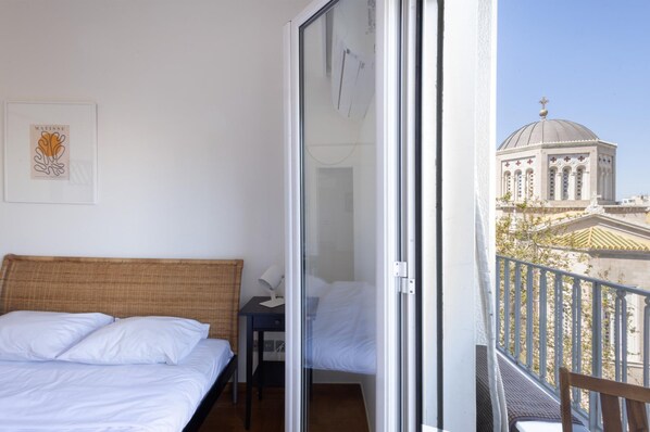 A hotel room with a bed, a small desk, and a balcony with a view of a building.