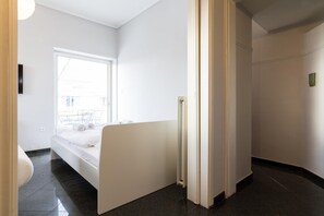 Una habitación de hotel moderna con un ventanal grande, una cama, un radiador y una puerta que da a otra habitación.