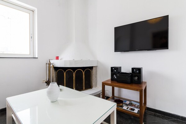 Una sala de estar moderna con una chimenea blanca, un televisor de pantalla plana montado en la pared y una mesita de madera con altavoces.