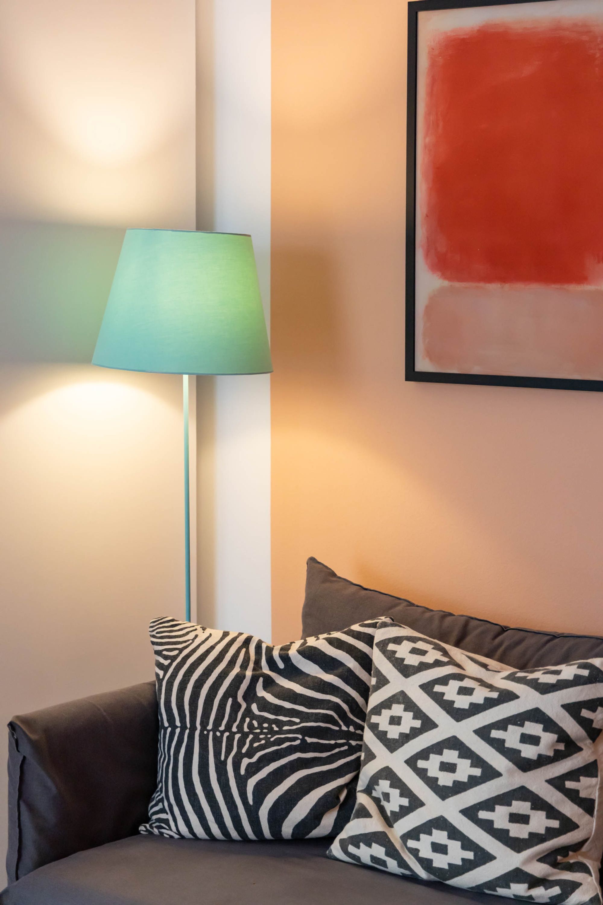 A modern room with a floor lamp, two patterned pillows, and a framed abstract painting.