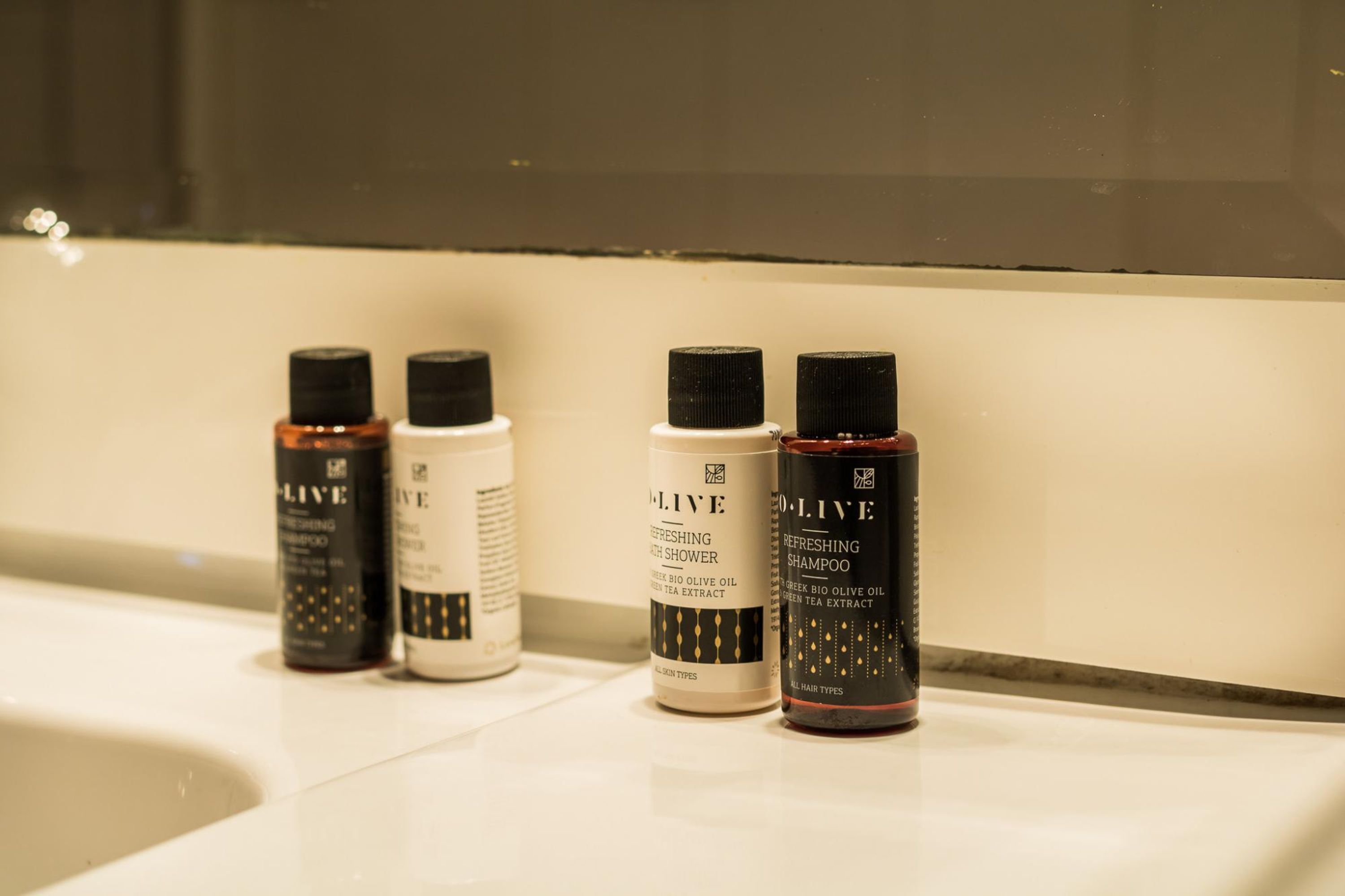 A row of olive oil shampoo bottles on a bathroom counter.