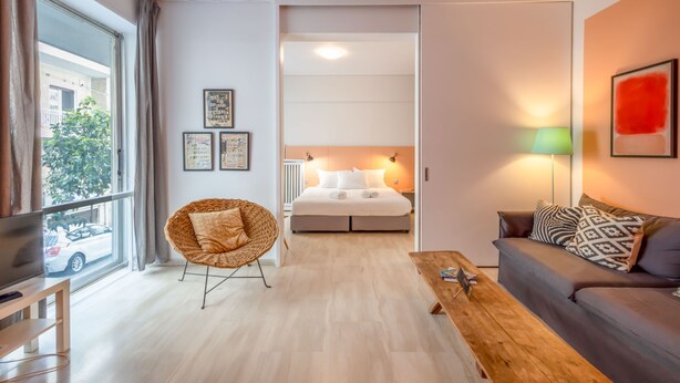 A modern hotel room with a large window, a bed, a sofa, a wooden coffee table, and a wicker chair. - Elegant Retreat in Kolonaki - Renovated April 2026 (Athens)