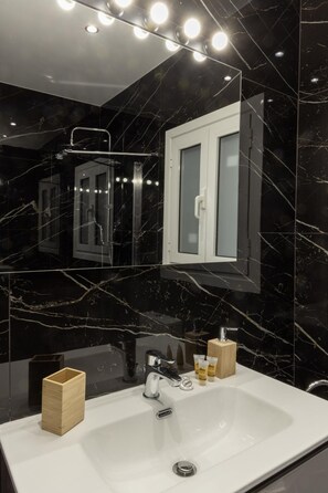 A modern bathroom with a large mirror, a white sink, and a wooden container.