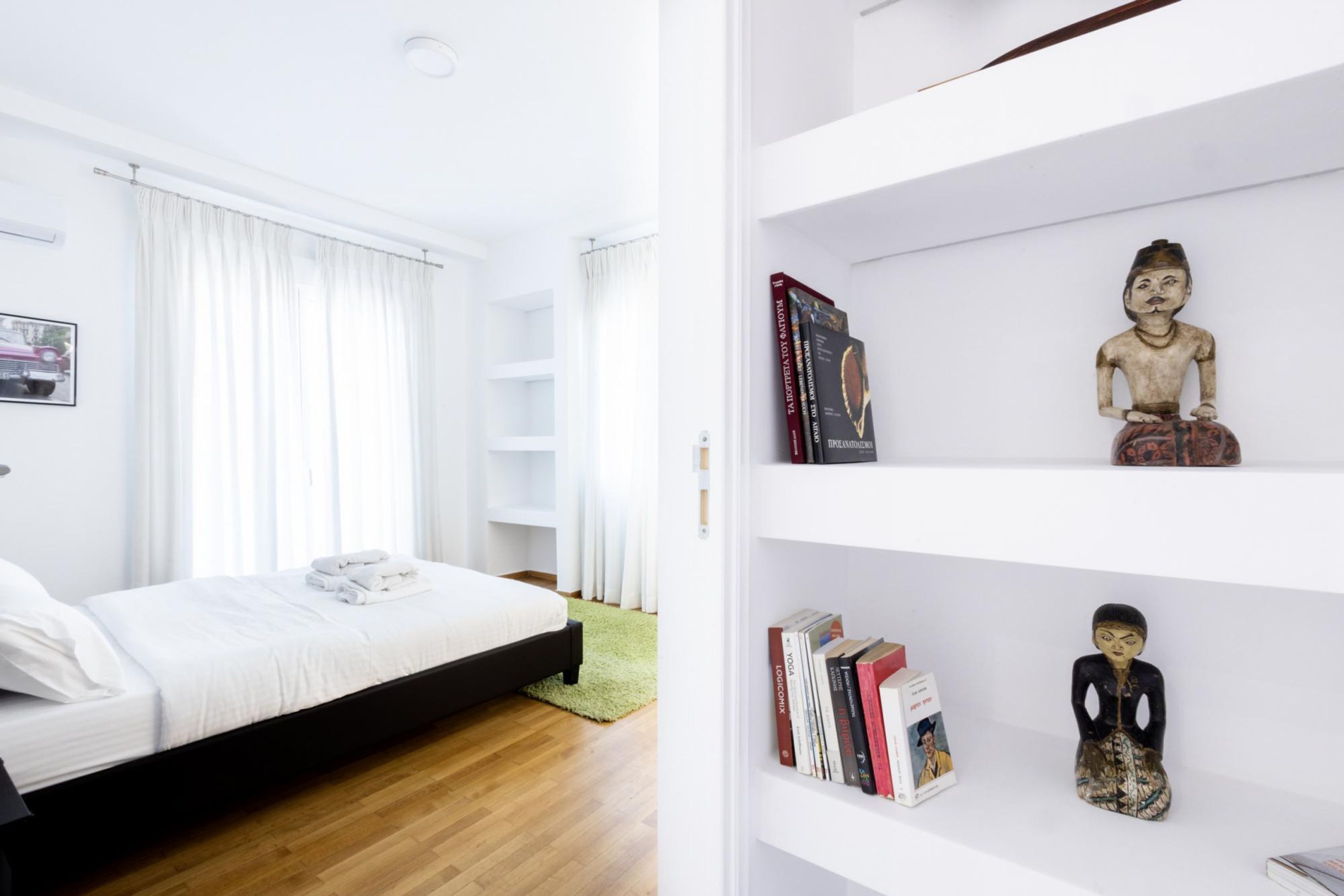 A modern bedroom with a bed, a bookshelf, and a small statue.