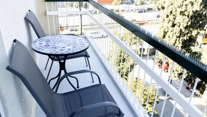 A balcony with a round table and two chairs, a white railing, and a view of a street with cars and trees. - Beautiful 2 Bdrm apt in Athens (Athens)