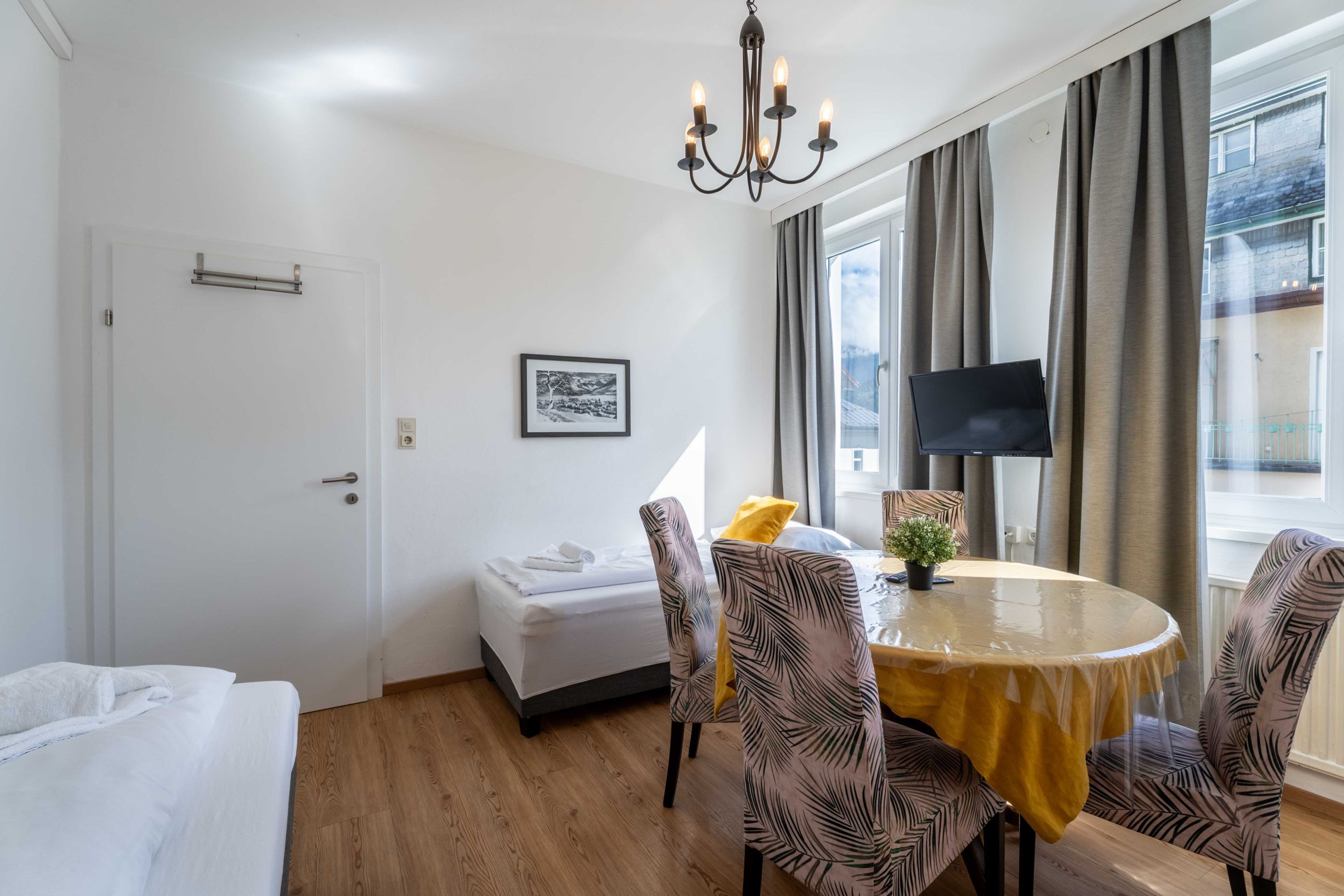 Ein Zimmer mit einem Bett, einem Esstisch mit Stühlen, einem Fernseher und einem Fenster mit Vorhängen.