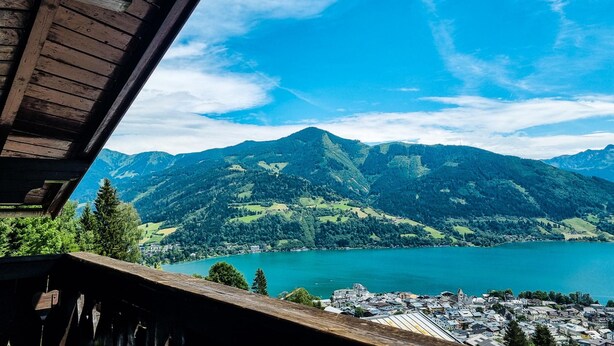 A view from a wooden balcony overlooking a lake and mountains. - Apartment Bauernhof Birkh fl - TOP 1 (Zell am See)