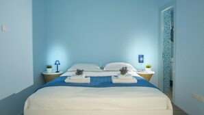 Un dormitorio con una cama, dos mesitas de noche con lámparas y una puerta que da a otra habitación.