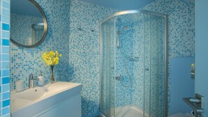 Un baño con cabina de ducha de vidrio, lavamanos con artículos de aseo y un espejo.