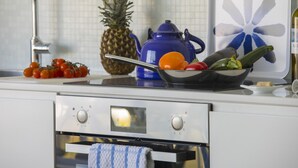 Una cocina con un horno de acero inoxidable, una tetera azul y un bol de verduras sobre la encimera.