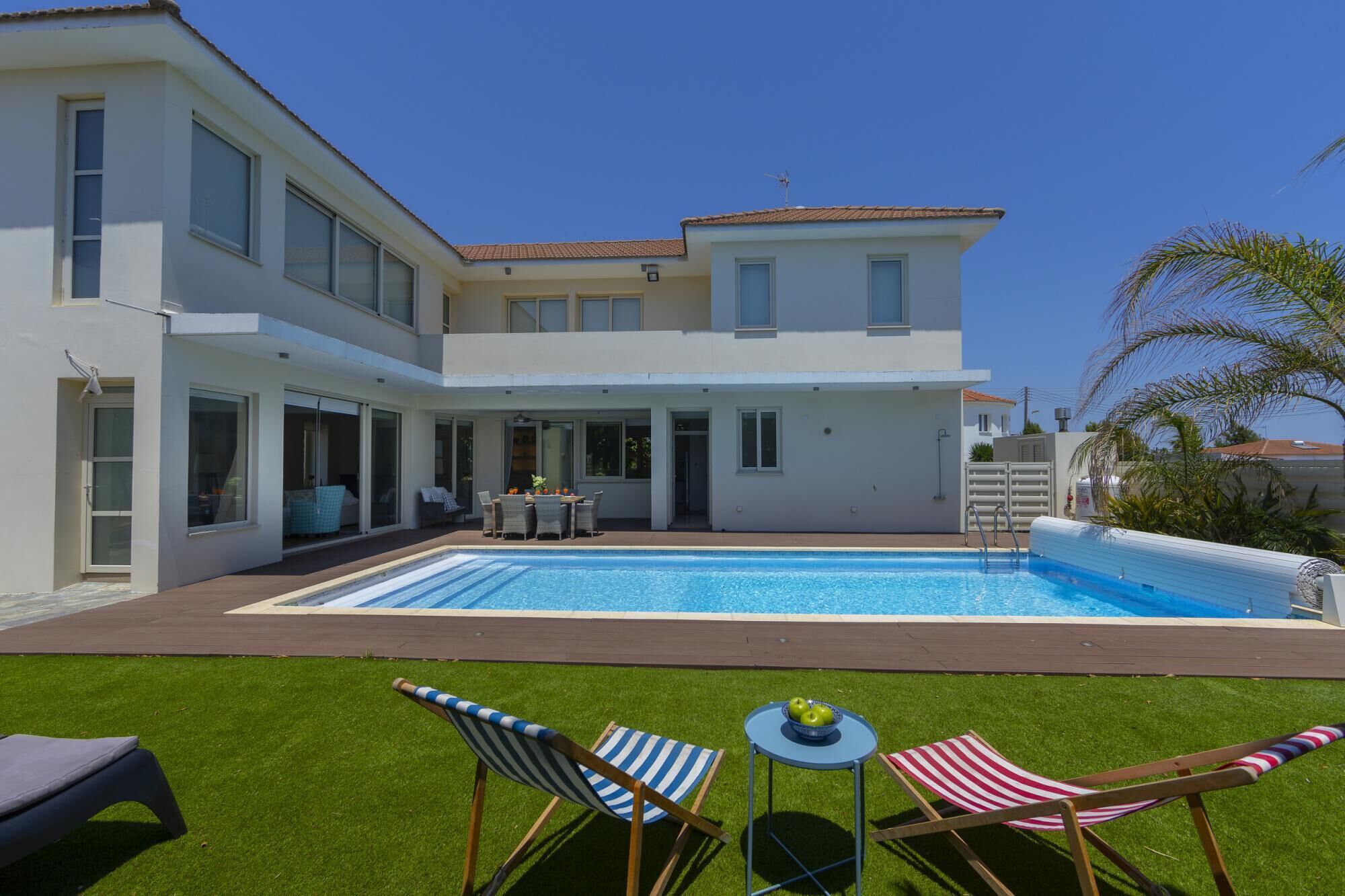 A modern two-story house with a swimming pool, outdoor seating, and a well-maintained lawn.