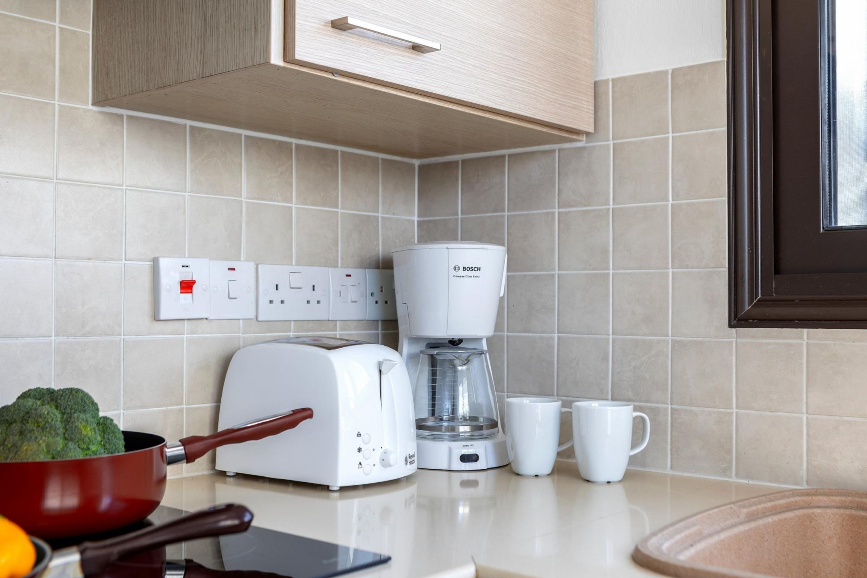 Une cuisine moderne équipée d’une machine à café Bosch, d’un grille-pain et d’un bol de brocolis posé sur le comptoir.