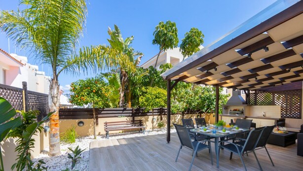 An outdoor patio with a pergola, dining table, chairs, and a grill area. - Protaras Villa Angela Nefeli (Paralimni)