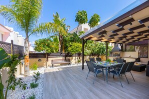An outdoor patio with a pergola, dining table, chairs, and a grill area. - Protaras Villa Angela Nefeli (Paralimni)
