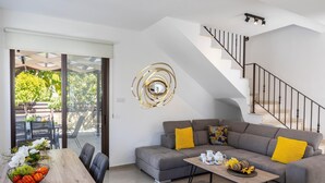 A modern living room with a grey sofa, yellow cushions, a wooden coffee table, and a staircase. - Protaras Villa Angela Nefeli (Paralimni)