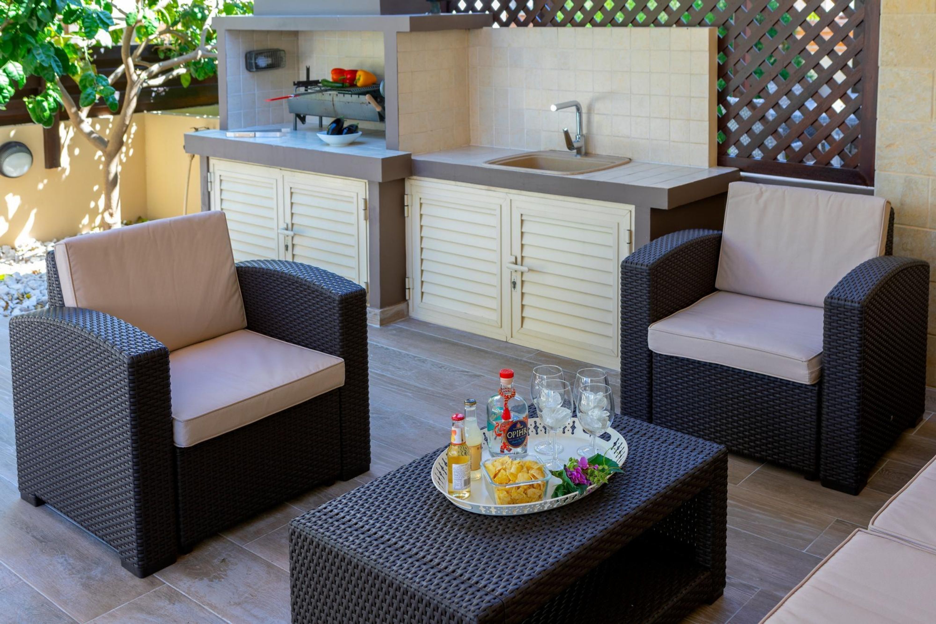 An outdoor kitchen area with wicker furniture, a tray with drinks and snacks, and a sink.