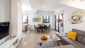 A modern living room with a flat-screen TV, a sofa with a yellow pillow, and a dining area with a table and chairs. - Protaras Villa Angela Nefeli (Paralimni)