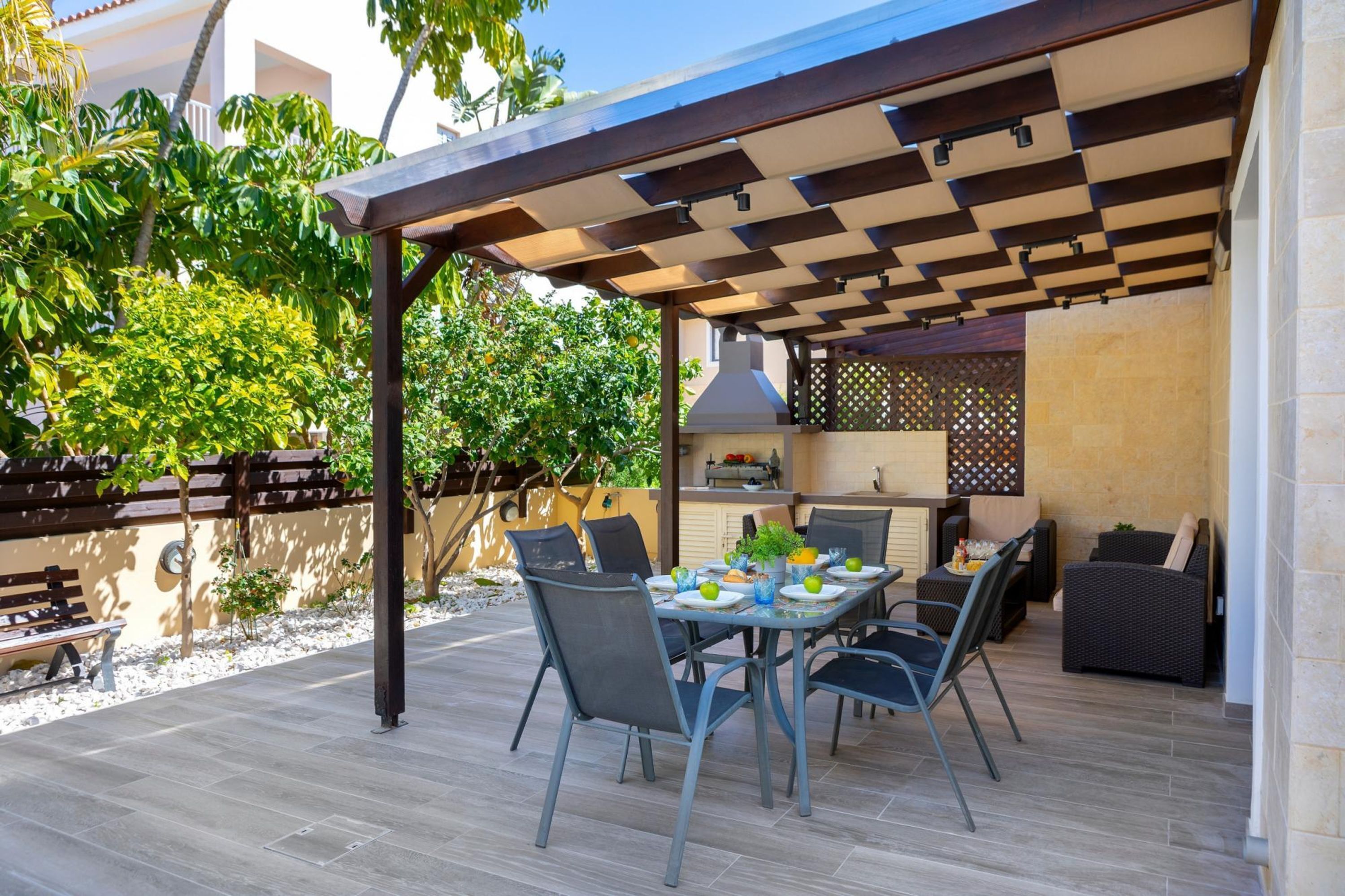 Eine Terrasse im Freien mit einer Pergola, einem Esstisch, Stühlen und Grillplatz.