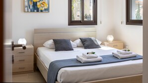 A neatly made bed with a blue blanket, two pillows, and a bedside table with a lamp. - Protaras Villa Angela Nefeli (Paralimni)