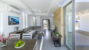 A modern living room with a sectional sofa, a dining table with a bowl of fruit, and a stone accent wall. - Protaras Villa Mylos 9 (Paralimni)