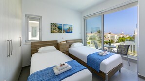 A hotel room with two beds, a balcony with a view of the city, and a painting on the wall. - Protaras Villa Mylos 9 (Paralimni)
