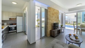 A modern kitchen with a built-in oven, a dining area with a round table, and a stone fireplace. - Protaras Villa Mylos 9 (Paralimni)