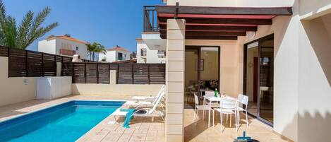 A poolside area with a pool, lounge chairs, a barbecue grill, and a patio table.