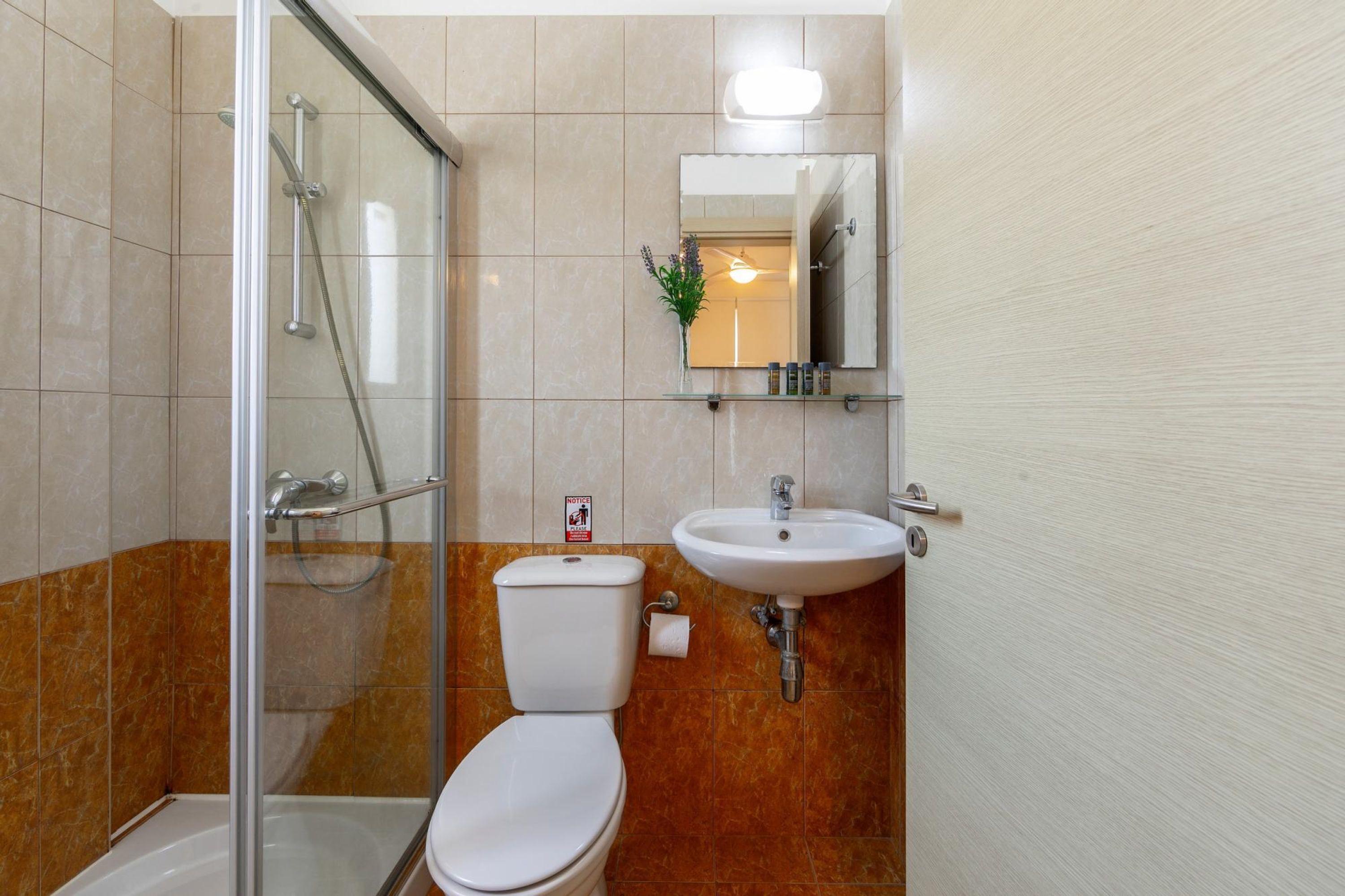 A bathroom with a glass shower enclosure, a white toilet, and a sink with a mirror above it.