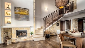 A spacious living area with a stone fireplace, a staircase with a metal railing, and a dining table set with chairs. - Palmrise Luxury Villas - Blue Villa (Kassandra)
