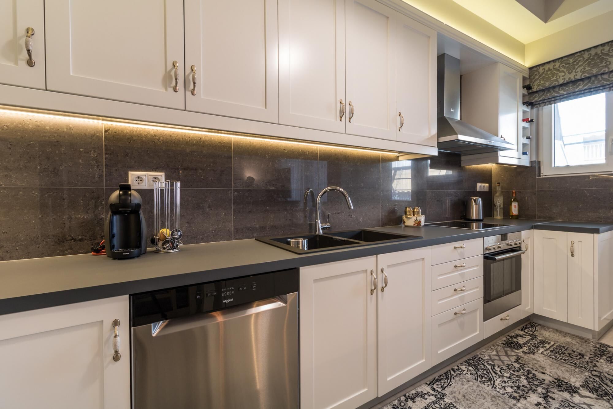 A modern kitchen with white cabinets, a stainless steel dishwasher, and a black countertop.