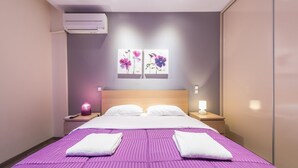 Een hotelkamer met een groot bed, twee nachtkastjes, een wandairconditioner en twee kunstwerken aan de muur.