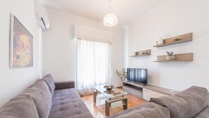 Ett modernt vardagsrum med en soffa, ett soffbord, en tv och dekorativa hyllor.