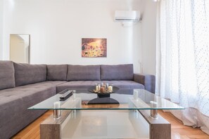 Uma sala de estar moderna com um sofá cinzento, uma mesa de centro de vidro e um quadro na parede.