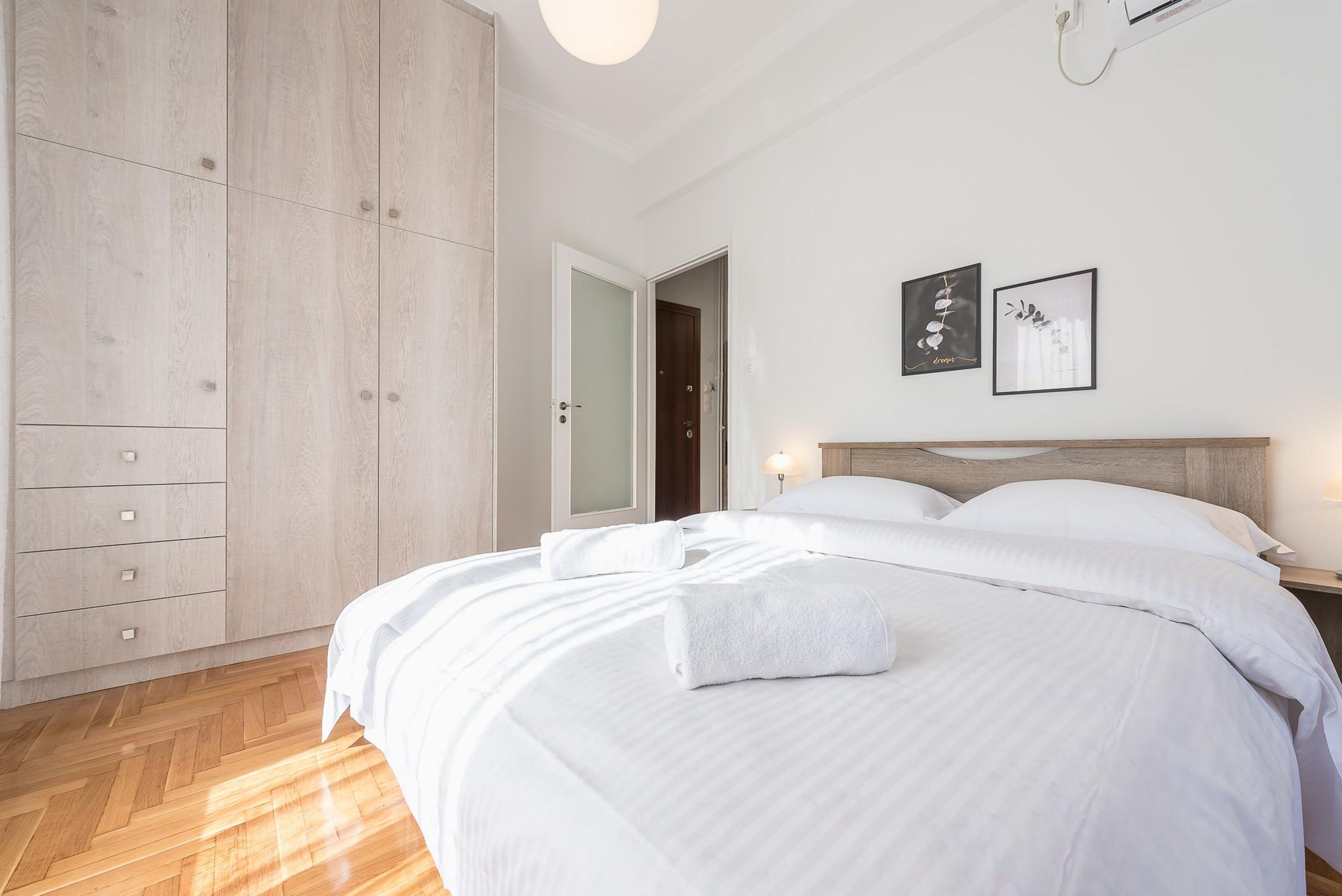 A bedroom with a large bed, a wardrobe, and two framed pictures on the wall.